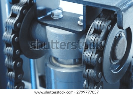 Two parallel metal chains hang vertically inside machine. Cylindrical shaft divides frame. Exposed wiring mechanical parts fill background tech industrial technology background