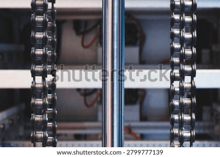 Two parallel metal chains hang vertically inside machine. Cylindrical shaft divides frame. Exposed wiring mechanical parts fill background tech industrial technology background