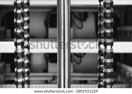 Two parallel metal chains hang vertically inside machine. Cylindrical shaft divides frame. Exposed wiring mechanical parts fill background tech industrial technology background
