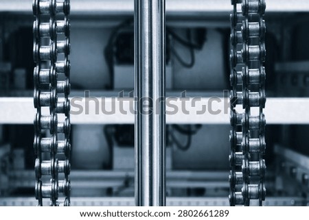 Two parallel metal chains hang vertically inside machine. Cylindrical shaft divides frame. Exposed wiring mechanical parts fill background tech industrial technology background