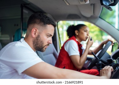 Two Paramedics In The Front Of An Ambulance. The Focus Is On The Man, A Young Man In His 20s Looking Through The Open Driver's Side Window.