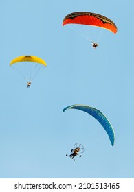 Two Paramotor Glider and One Paratrike Flying in a Blue Sky