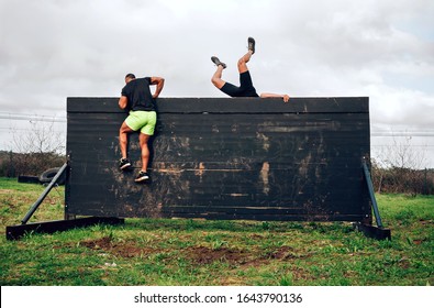 Two Participants In An Obstacle Course Climbing A Wall