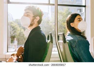 Two Passengers, Man And Woman Sitting Back To Back To Each Other On Urban Public Transport. Caucasian People Go To Work Or Study By Public Transport. Face Mask Protection Against Virus.