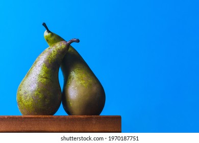 Two pears are sitting on the edge of a wooden table, hugging each other. Blue background.