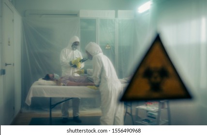 Two people attending to a woman with a virus lying on a stretcher in a field hospital with bio hazard symbol in the foreground - Shutterstock ID 1556490968
