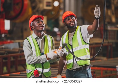 Two people black man African American worker control heavy machine in the factory. - Shutterstock ID 2140043827