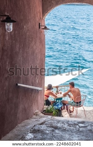 Two people at a cafe table on the shore of the Adriatic Sea and the arch of the building.