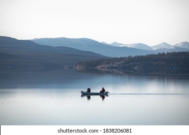 Two People Canoing Over A Clear, Calm And Stunning Lake Surrounded By Mountains And Wilderness In Northern Canada. 