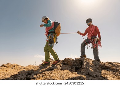 Two people are climbing a mountain, one of them is wearing a backpack. The other person is holding a rope - Powered by Shutterstock