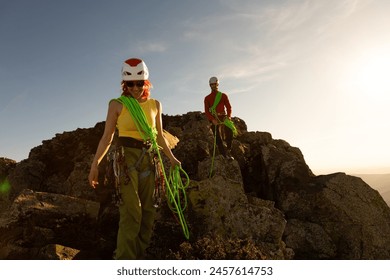 Two people are climbing a mountain, one of them wearing a yellow shirt. The woman is holding a green rope, and the man is holding a green rope as well. The scene is bright and sunny - Powered by Shutterstock