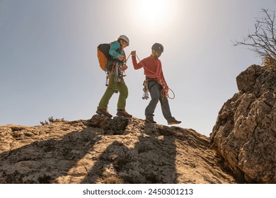 Two people are climbing a mountain together. One of them is wearing a red shirt. The other person is wearing a backpack - Powered by Shutterstock