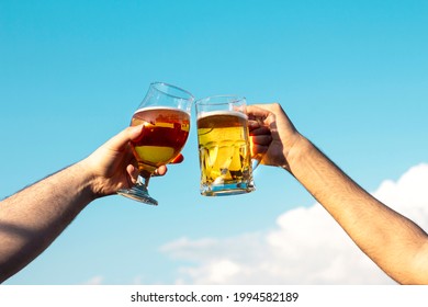 Two people clinking beer glasses outdoors.Two friends toasting or cheering with beer at terrace,the sky appears in the background.
