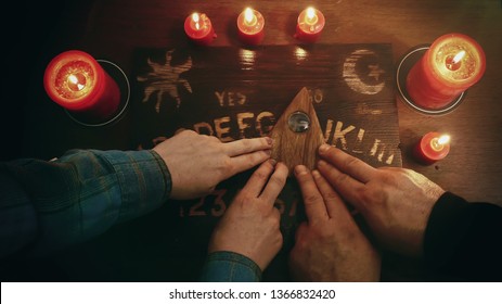 Two people conducting a seance using a Ouija Board, or Talking Spirit Board, with red candles. Shot from overhead.