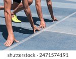 Two people are crouched at the starting line ready to run at the start of a race on a track. The track is blue and white. Concept of determination and focus.