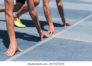 Two people are crouched at the starting line ready to run at the start of a race on a track. The track is blue and white. Concept of determination and focus. - Powered by Shutterstock