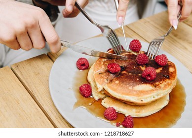 Two people cutting into a stack of delicious fluffy American pancakes with raspberries and Marple syrup