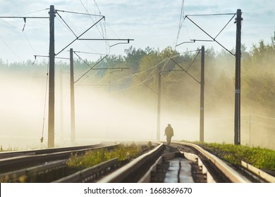 Two people in dense fog are walking along the railway tracks. Lonely travelers go into the distance. Misty morning on the railway. Railroad tracks go beyond the horizon. Green trees in the background - Powered by Shutterstock