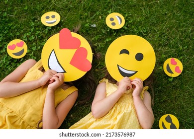 Two people with different cardboard smiles cover their faces lying on the grass. Lover and winking emoticons, top view