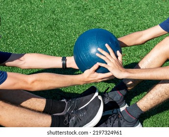 Two People Doing Sit Ups Passing A Medicine Ball To Each Other On A Turf Field.