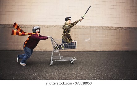 Two People Dressed Up As Super Heroes Or Characters Horsing Around In A Shopping Cart With Goggles And A Helmet And Sword