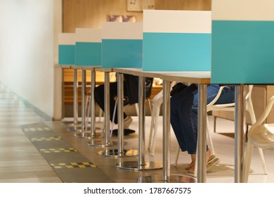 Two People Eating At Food Court In Shopping Mall With Blue Plastic Table Barrier Separate Each Customers Apart After Reopening From Lockdown. New Normal & Physical Distancing During Covid-19 Pandemic.