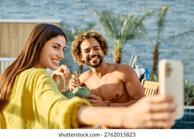 Two people enjoy coconuts while sitting in water at a pool area and using a smartphone camera  taking a selfie photo in a warm location during summer