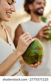 Two people enjoy coconuts while sitting in water at a pool area in a warm location during summer