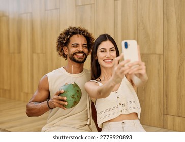 Two people enjoy coconuts while sitting in water at a pool area and using a smartphone camera  taking a selfie photo in a warm location during summer