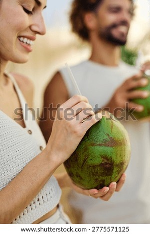 Two people enjoy coconuts while sitting in water at a pool area in a warm location during summer