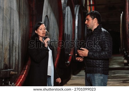 Two people enjoy wine while discussing flavors inside a traditional winery.