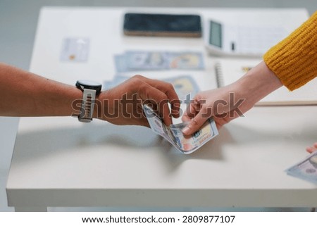 Two people are exchanging US dollar banknotes, showing concepts of payment, salary, debt, investment, or a financial agreement between individuals on a clean table