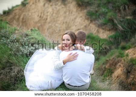 
two people, a happy couple in love, a man and a woman with a beautiful make-up and red lips, walking in the nature against the backdrop of the sea along the green grass on the slopes of the mountains