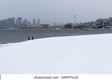 Two People In Heavy Coats Stand In Front Of Lake Union In Seattle Washington With Space Needle In View On A Rare Snowy Day