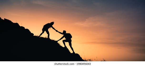 Two people helping each other climb up a mountain. Giving a helping hand,  and adventurous active lifestyle concept. 