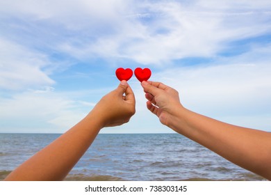 Two people hold two red hearts with background sky and sea.