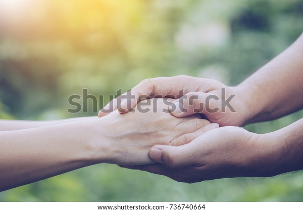 Two people holding\
hand together over blurred nature background,Business man and woman\
shaking hands,helping hand  and world peace concept with copy\
space