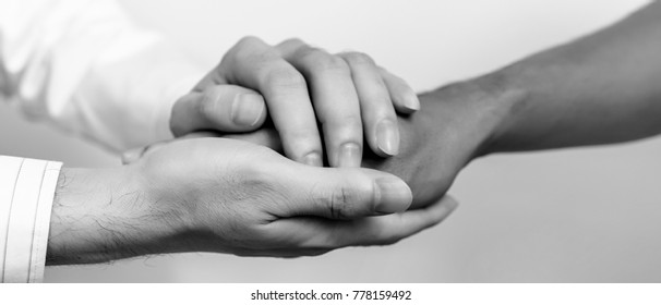 Two People Holding Hands For Comfort. Doctor Consoling Relatives Of Patients In Hospital Concept. Black And White. Banner Panoramic Crop For Copy Space.