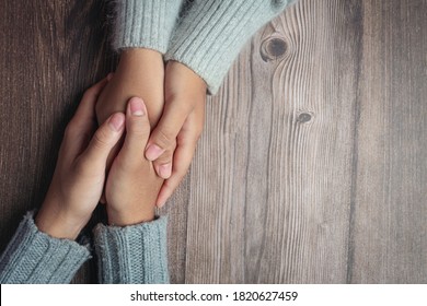Two people holding hands together with love and warmth on wooden table