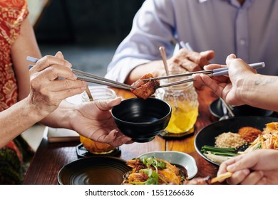 Two people holding one piece of deep fried chicken with chopsticks and trying to dip it in soy sauce