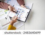 Two people are looking at a graph on a table. One of them is holding a calculator. The graph shows a comparison of different data points