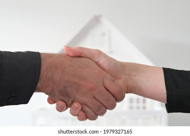 Two People (male And Female) Are Shaking Hands Against A White House. Mortgage, Housing Market, Home Loans And Property, Management Concept. No People. Copy Space