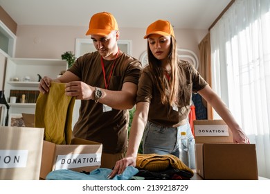 Two People Man And Woman Couple Volunteers Preparing Donation For Charity Happy Volunteer Working In Charitable Foundation Separating And Sorting Stuff Putting Clothes In Boxes