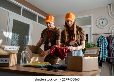 Two People Man And Woman Couple Volunteers Preparing Donation For Charity Happy Volunteer Working In Charitable Foundation Separating And Sorting Stuff Putting Clothes In Boxes