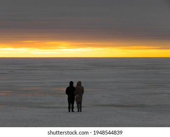 Two people a man and a woman look at the winter sunset under a heavy leaden sky as if it were the end of the world