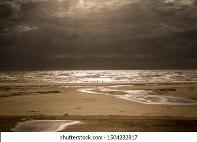 two people on the beach on a stormy day with sun rays breaking through the clouds.