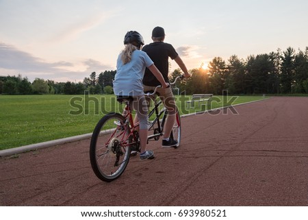 Two people on a tandem bike looking at the sunset. 