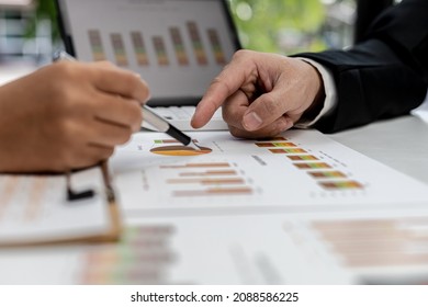 Two people pointing to a company financial summary, two businessmen brainstorming ideas to resolve losses and planning strategies to keep the company profitable and growing.