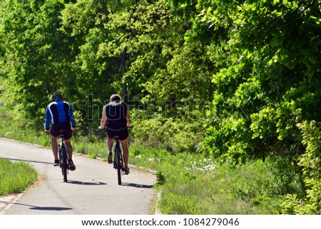 Two people ride a bicycle on a recreational trail