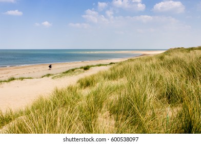 Two people with rucksacks walking down a sandy beach on a sunny day in Burnham Overy Staithe, Norfolk, England, UK.